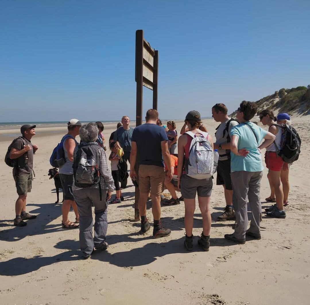 Groupe de géocacheurs rassemblés autour d'un panneau sur une plage